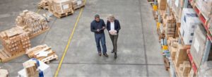Arial view of two colleagues discussing while looking at a tablet in a warehouse