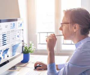 A female professional looking at graphs on her desktop while working from her office desk across a bright window