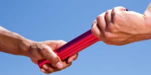 Close up of a male athlete passing a relay baton to his teammate on a bright sunny day at an athletics competition