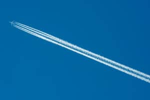 Airplane ascending upwards with contrails in a clear blue sky