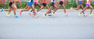 Lower half of multiple runners in colorful running shoes and shorts during a race