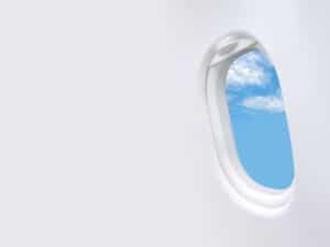 An open airplane window on a white wall showing blue cloudy skies